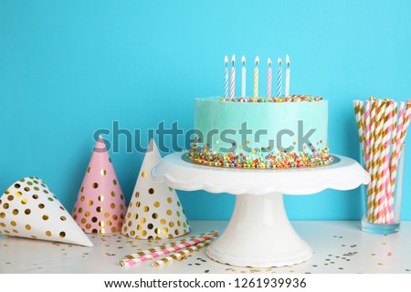 Fresh delicious cake and birthday caps on table against color background. Space for text