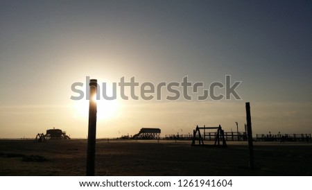 
a wooden post hiding the evening sun at the beach in Sankt Peter-Ording
