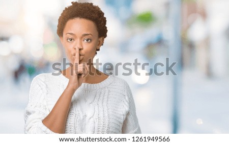 Beautiful young african american woman wearing sweater over isolated background asking to be quiet with finger on lips. Silence and secret concept.