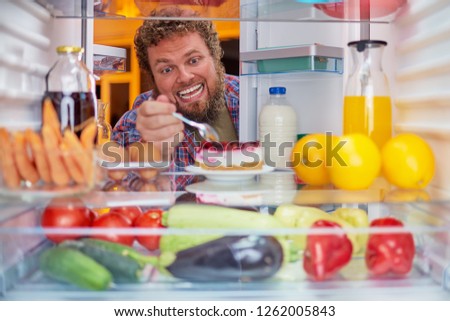 Man eating cheesecake. Unhealthy eating concept. Picture taken from the inside of fridge full of groceries.