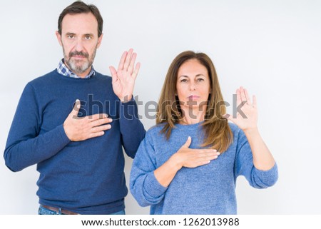 Beautiful middle age couple in love over isolated background Swearing with hand on chest and open palm, making a loyalty promise oath