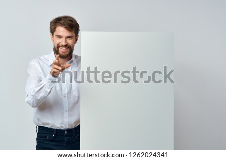A cheerful man in a white shirt is holding a mockup in his hand      