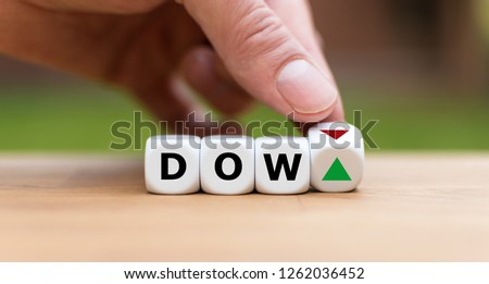 Hand is turning a dice and changes the direction of an arrow symbolizing that the Dow Jones Index is changing the trend and goes up instead of down (or vice versa) Royalty-Free Stock Photo #1262036452