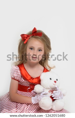 Lovely little girl in a very short white summer dress sits on her knees on the floor and hugging a Teddy bear .