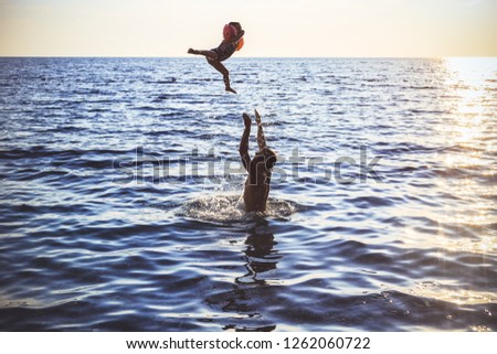 Father and daughter are in the sea evening time. Little girl jumps in the sea from father's hands. Concept of friendly family.