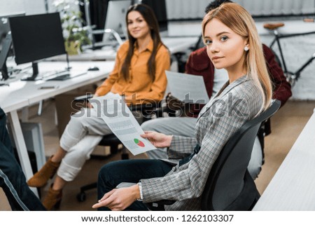 selective focus of young businesswoman with papers near multiracial colleagues at workplace in office