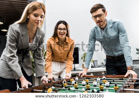 cheerful business colleagues playing table football together in office