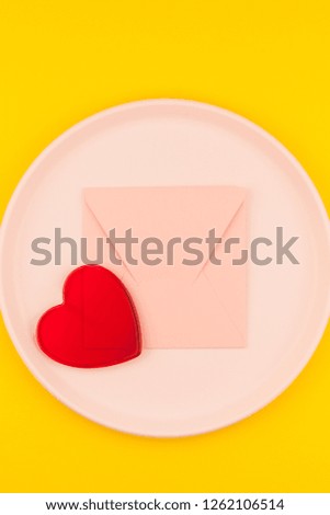 Small love pink letter on plate with serving plastic tableware with copy space on bold yellow background in creative minimal style. Concept template for Valentine holiday feminine blog social media