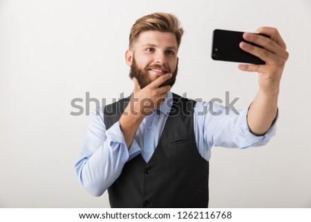 Picture of a handsome young bearded man standing isolated over white wall background take a selfie by mobile phone.