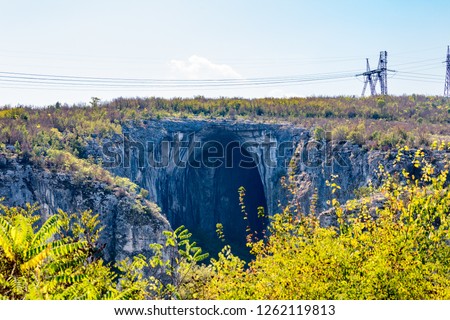 The huge entrance of the Prohodna cave in Northern Bulgaria, electric poles and wires on top, an example of juxtaposition