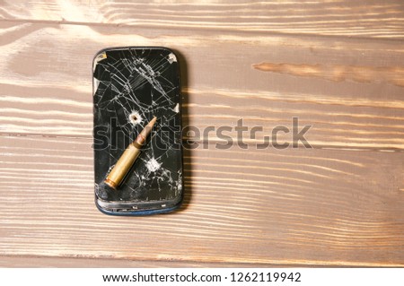 Crashed black smartphone with a bullet on white background. Broken lcd touch screen. Information technology photo. War concept.