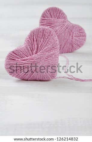 Two pink clews in shape of heart on white wooden background