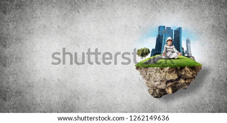 Young little boy keeping eyes closed and looking concentrated while meditating on flying island in the air with gray wall on background. 3D rendering.