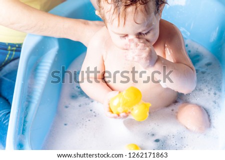 Mother washing little boy in a blue bath in the bathroom. Hygiene and the emotions of the baby while bathing
