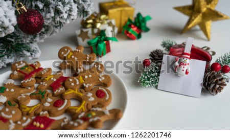 Christmas cookies of various shapes in sugar glaze on white plate. Card note for text with snow man. Christmas composition with gingerbread men and christmas tree