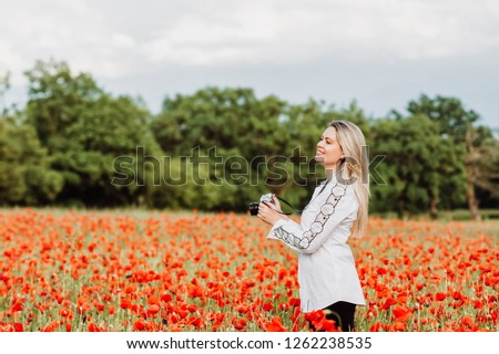 Beautiful woman photographer enjoying amazing day at poppy field, holding vintage film camera