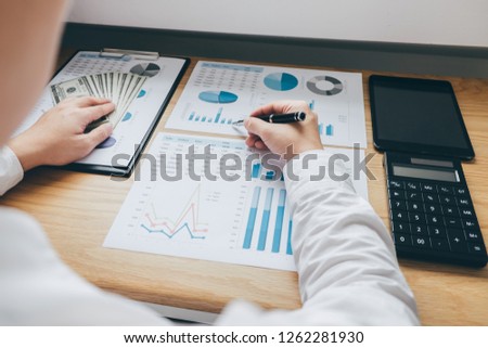 Businessman working on a graph document financial report and analysis calculation investment cost with calculator at office desk and other objects around.