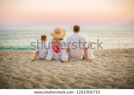 Photo of a large family in white closes on the beach. The family sits on the beach, ocean, sand image. Happy family on vacation, posing from the back without faces picture.