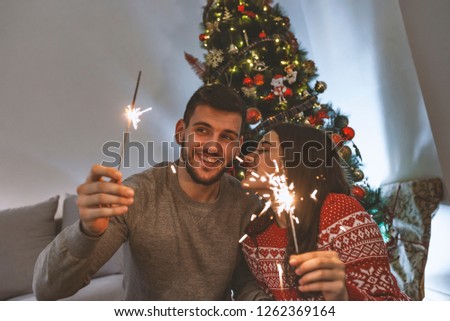 Picture of young couple hugging in Christmas time, Holding sprayers in their hands. Couple congratulates New Year with sprayers. Lovely couple holding Christmas sprinkler indoors