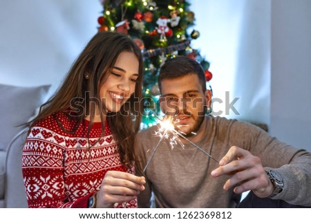 Picture of young couple hugging in Christmas time, Holding sprayers in their hands. Couple congratulates New Year with sprayers. Lovely couple holding Christmas sprinkler indoors