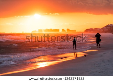 Young couple looking at dramatic orange red sunset in Santa Rosa Beach, Florida with Pensacola coastline coast skyline in panhandle with ocean gulf mexico waves