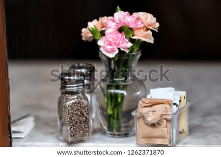 Closeup of salt, pepper and brown raw turbinado sugar shakers, packets, bottles on marble granite table, window in cafe restaurant, flowers in vase