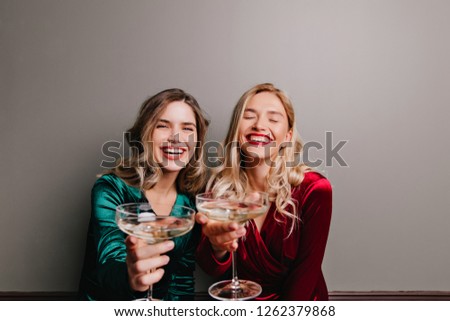 Fascinating caucasian girl in red velvet dress drinking champagne. Blissful friends celebrating something with wine.
