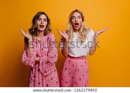 Surprised jocund women looking to camera with mouth open. Studio portrait of white girls expressing amazement on yellow backgorund.