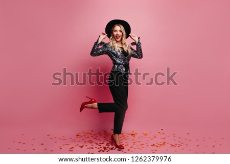 Full-length caucasian girl in black pants standing on one leg. Indoor shot of smiling glad woman in hat.