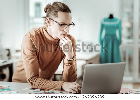 Lets think. Long-haired designer from generation Y wearing a brown garment looking concentrated
