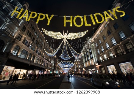 Happy Holidays message hanging in gold glitter letters in front of the Christmas lights of Regent Street in London on a winter night