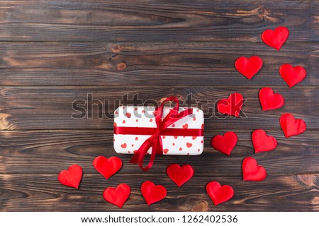 Valentine or other holiday handmade present in paper with red hearts and gifts box in holiday wrapper. Present box of gift on dark wooden table top view with copy space, empty space for design.
