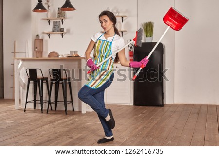 Funny picture of brunette holding scoop and broom in hands. She pretends it is swords. Girl is ready for battle.