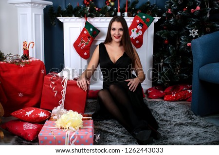 beautiful young woman in a long black dress on the background of the fireplace and Christmas and New Year's decor