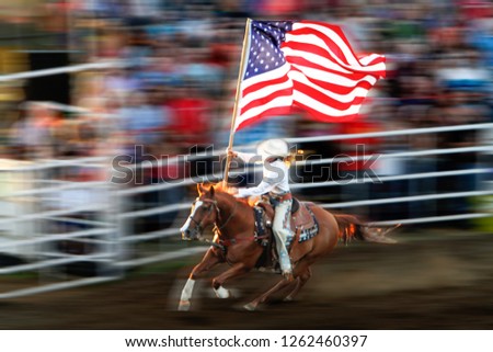 A young blond  woman riding a galloping horse with an American flag waving with motion blur