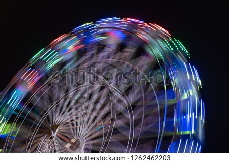 Colourful striped light illuminated spinning ferris wheel in motion moving at night.