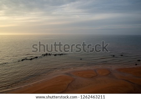 sandy sea beach with rocks and low tide in overcast day in autumn colors