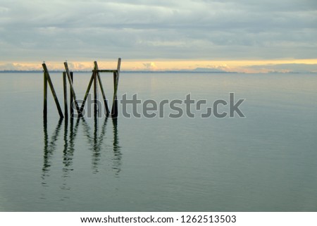remaining wooden piers standing on the calm river under heavy cloud near sunset
