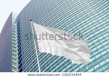 Blank white corporate flag on pole waving in the wind in the background of modern office building. Low angle colorful daytime picture 