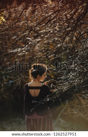 Autumn vibes. 4k. Gothic style. Brunette woman in dark red clothes stands with a mirror under tree with fallen leaves