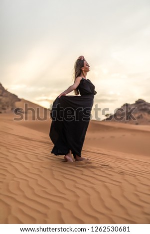 Portrait of beautiful young woman in long fluttering black dress posing at sandy desert