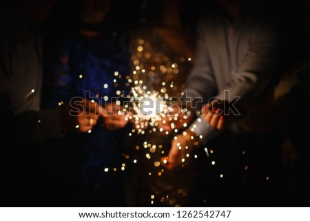 New year party burning sparkler closeup in hands on black background. company of people holding glowing holiday sparkling hand fireworks, shining fire flame. Christmas light.