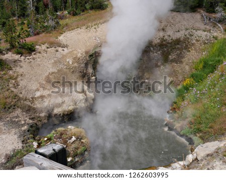 Medium wide shot of the Dragon's Mouth Spring with steam spewing out at Yellowstone National Park.
