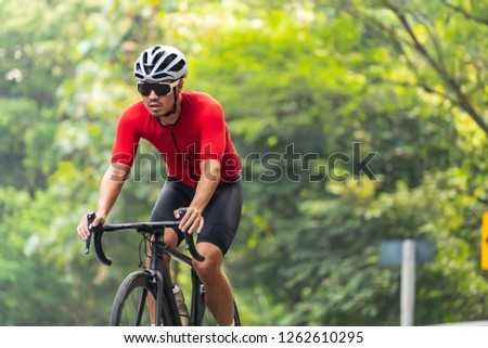 Asian man in red cycling jersey, white helmet and sun-glasses, riding on road bike on his way in the morning. exercise routine for good healthy. Royalty-Free Stock Photo #1262610295