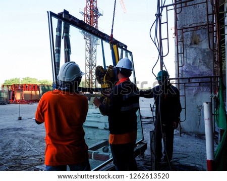 construction glass installtion construction workers installing glass wall of large building  Royalty-Free Stock Photo #1262613520