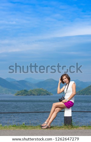 Women and the camera sitting on a concrete pillar at Kaeng Krachan dam phetchaburi , Thailand.