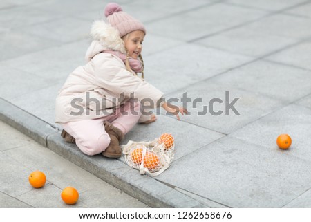 Cute little girl holding bag with fresh orange outdoor