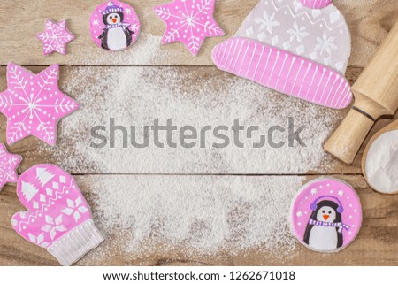 Christmas cooking. Flour for baking, rolling pin, ginger cookies in the form of penguins, mittens and hats with asterisks, on a wooden background. With free space for text. Festive background.