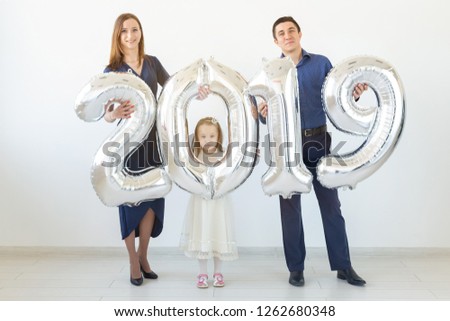 New 2019 Year is coming concept - Cheerful mother, father and daughter are holding silver colored numbers indoors.