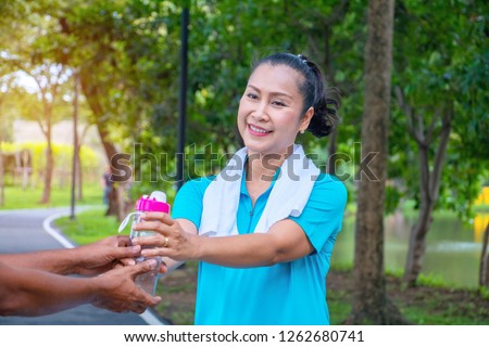Asian woman relax time in park. A man sent water for woman.She is drinking water.She is  smile and be happy in good time ,Life style,Photo concept  exercise and healthy.